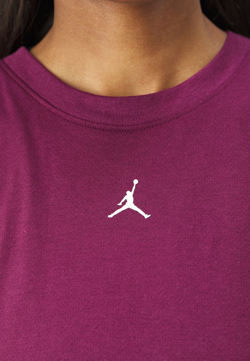 Nahaufnahme einer Person, die ein lila Hemd mit einer weißen Silhouette eines Basketballspielers in der Sprungmitte trägt, der einen Ball in der Mitte hält.