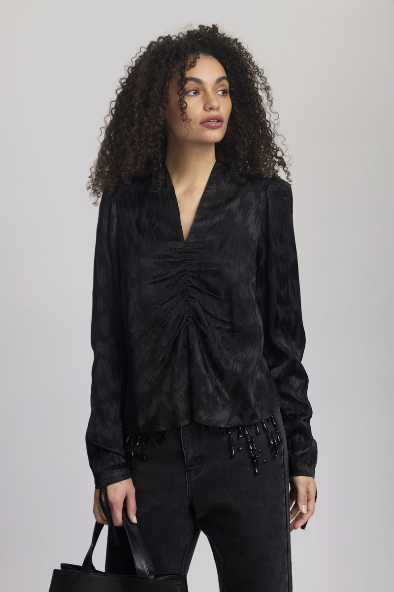 Blusa nera a maniche lunghe con scollatura a V e arricciature frontali, caratterizzata da un motivo testurizzato e dettagli di perline all'orlo, abbinata a jeans neri.