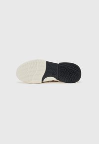 White and black sneaker sole with a textured black rubber pattern and a smooth cream rubber section, featuring zigzag tread for grip.