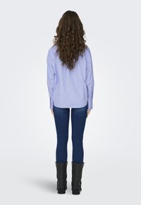 Camisa abotoada de riscas azul claro, com mangas longas, combinada com jeans de ganga escura e botas de couro pretas até ao joelho.