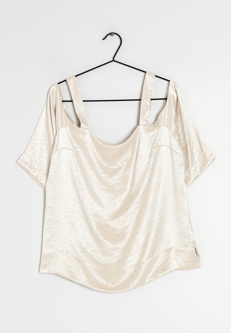 Top beige chiaro su una gruccia nera, con ampie maniche scese sulle spalle, un frontale drappeggiato e una texture lucida e liscia.