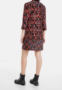 Šaty s květinovým vzorem na černém pozadí s červenými a růžovými designy. V kombinaci s černými vojenskými botami a žebrovanými manžetami.