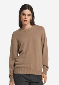 Beżowy sweter robiony na drutach z okrągłym dekoltem, ściągaczami przy mankietach i u dołu. Wykonany z miękkiej tkaniny, charakteryzujący się luźnym krojem i długimi rękawami.