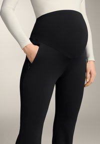 Black maternity leggings with a high waistband featuring a smooth texture, side pockets, and fitted design.