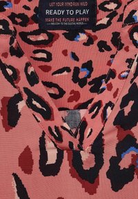 Haut en tissu rose avec un décolleté en V, featuring un motif léopard en noir, rouge foncé et bleu, et une étiquette avec des informations de marque.