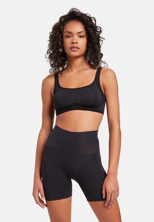 Zwarte sport-bralette met brede banden en middellange fietsshorts. Gladde textuur, minimale naden, ontworpen voor comfort en beweging.