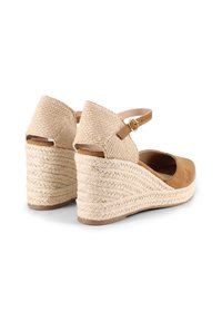 Sandalias de cuña de ante marrón con un tacón de yute trenzado, tira en el tobillo con hebilla y punta redondeada. Tejido beige texturizado en el tacón.