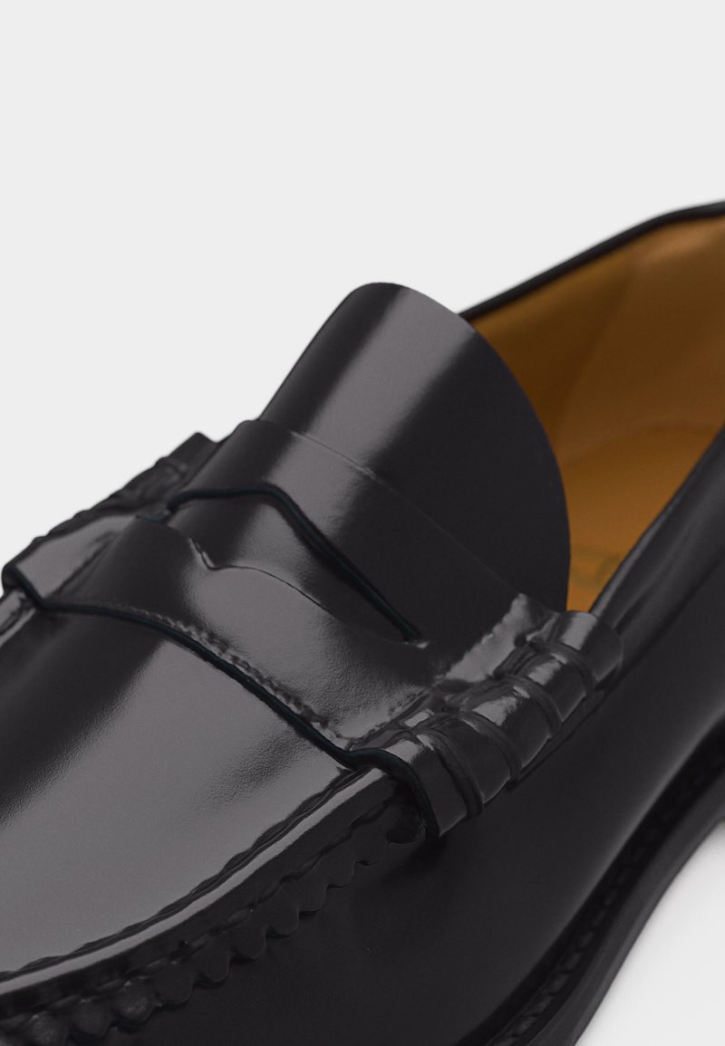 Mocassin en cuir noir poli avec lanière penny et couture moc toe, doté d'une doublure intérieure beige.