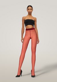 Leggings rossi semi-trasparenti con una vita rossa uniforme, abbinati a un top nero senza spalline, indossati con tacchi alti neri. Texture liscia.