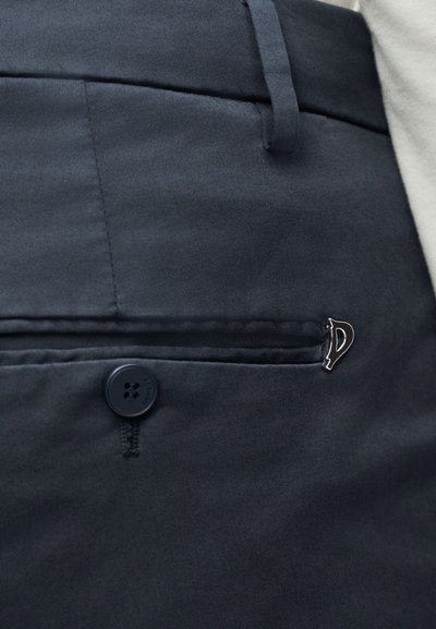 Σκούρο μπλε σκούρο παντελόνι με τσέπη στο πίσω μέρος που διαθέτει κουμπί και μικρό ασημί γάντζο στο χείλος της τσέπης.