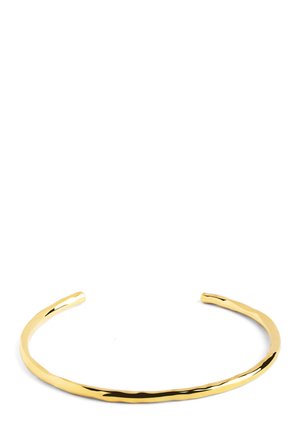 Cienka, nieregularnie ukształtowana błyszcząca złota bransoleta mankietowa z otwartym projektem na białym tle.