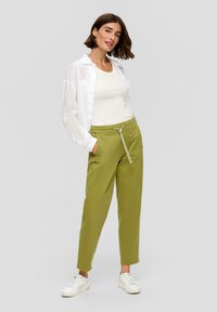 Pantalons olive verts avec taille à cordon, design à jambe droite et poches avant, associés à un débardeur blanc et une chemise légère blanche.