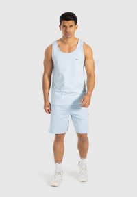 Lichtblauw tanktop en shorts van zachte stof, met een klein logo op de borst en zoom, gecombineerd met witte sneakers en sokken.