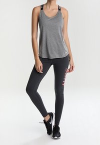Grå atletisk tanktop med sorte stropper, der viser mærkenavnet, sammen med sorte leggings, der viser et rosa logo. Sorte sneakers fuldender outfittet.