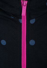 Tessuto nero con pois blu, dotato di una cerniera rosa. La vista ravvicinata mette in evidenza la texture della cerniera e il contrasto di colori.