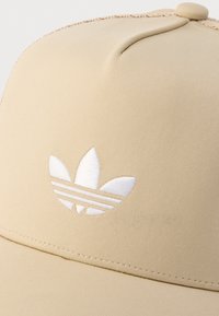 Μπεζ καπέλο μπέιζμπολ με λευκό κεντητό λογότυπο Adidas trefoil στο κέντρο της μπροστινής πλευράς.