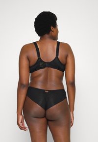 Sostenedor de encaje negro con tirantes ajustables y cierre de gancho. Panties negros sin costuras con un pequeño detalle de ojal en la parte posterior, textura suave.