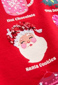 Tessuto rosso con il disegno testurizzato del volto di Babbo Natale, caratterizzato da paillettes e testo bianco con le scritte "Hot Chocolate" e "Santa Cookies".