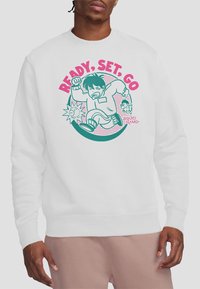 A person wears a white sweatshirt featuring a cartoon child running with the text "READY, SET, GO" and playful graphics, inspired by "Squid Game."