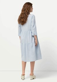 Vestido azul claro, de longitud hasta la rodilla, con mangas de tres cuartos, diseño en capas y corte en el hombro trasero, fabricado con una tela suave y texturizada.