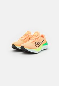 Une paire de chaussures de course Nike orange avec un swoosh noir, une semelle verte et blanche, présentée sur un fond blanc à un léger angle.