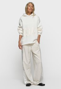 Sudadera blanca extragrande con "TODAY" en beige claro. Combinada con pantalones gris claro con acentos de satén en los costados. Calzado negro completa el conjunto.