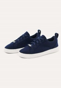 Marineblaue Canvas-Sneaker mit einer flachen weißen Gummisohle, Schnürdesign und einem Zugtab am Fersenbereich. Weiche Textur mit minimaler Detailierung.