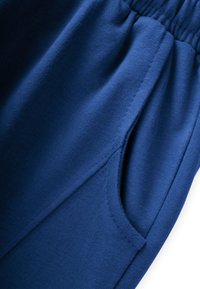 Mėlynos medvilnės sportinės kelnės su elastinga juosta ir šoninėmis kišenėmis, turinčios lygų paviršių ir minimalų siuvimo detalių kiekį.