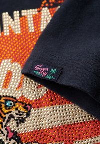 Marinblå bomulls t-shirt med ett färgglatt tigermotiv med rhinestone-accenter och en liten "Super Fly" logotyp som är sydd på fållen.