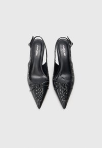 Chaussures slingback noires à talon aigu, avec un détail de laçage à l'avant et de petites clous en argent sur les côtés, exposées côte à côte sur un fond blanc.