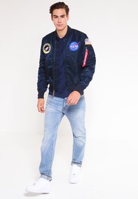 Tumesinine pommitaja jope NASA plaastritega, soonikute ääristega ja punase sildiga; koos helesiniste teksade ja valgete tossudega, luues mõnusa igapäeva välimuse.