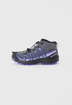 Chaussure de randonnée montante noire et violette avec tige en synthétique, finition texturée, accents réfléchissants et système de fermeture élastique.
