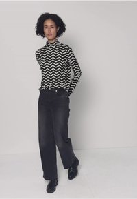 Musta-valkoinen siksak-kuvioitu pitkähihainen paita, yhdistetty korkeavyötäröisiin mustiin leveälahkeisiin farkkuihin ja mustiin nilkkureihin.