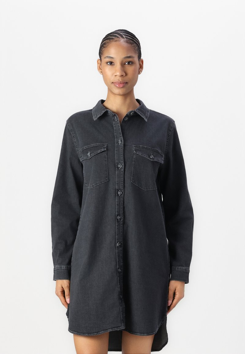 Black denim shirt dress with long sleeves, front button closure, two chest pockets, and a curved hemline. Textured fabric with a casual fit.