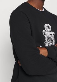 Sweat-shirt noir à col rond, avec un motif graphique blanc. Confectionné en tissu doux, avec des poignets ajustés et un ourlet côtelé.