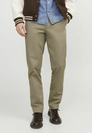 Pantalones caqui de tela suave, con un diseño ajustado. Combinados con zapatos oscuros de cordones y una camisa de mezclilla en contraste.