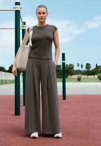 Haut gris à manches courtes côtelé associé à un pantalon gris ample taille haute. Un sac fourre-tout crème et des baskets blanches complètent la tenue.