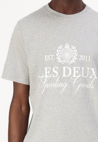 Tricou din bumbac gri cu mânecă scurtă, având inscripționat în alb textul: "LES DEUX Sporting Goods," "EST. 2011," și un design circular al logo-ului.