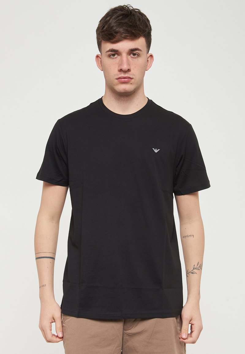 T-shirt noir à manches courtes en coton doux, avec un logo discret sur la poitrine gauche et un col rond. Texture lisse.