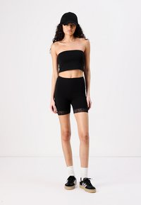 Svart stroppeløs topp og matchende høy midje shorts med blonder. Stilt med en svart caps og svarte joggesko med hvite detaljer.