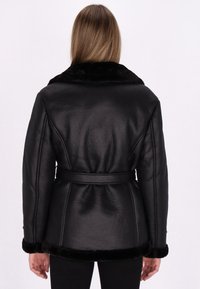 Veste en cuir noir avec une finition texturée, dotée d'un col et de poignets en fausse fourrure, ceinturée à la taille et d'une coupe ajustée.