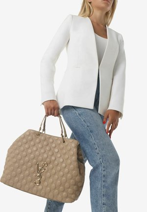 Borsa beige con un motivo a bolle testurizzato, doppi manici e hardware dorato. Abbinata a un blazer bianco e jeans in denim.