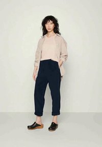 Heledbeige nööbiga särk roosa pluusi peal, kombineeritud tumedate, lõdva lõikega pükstega ja mustade puukingadega, millel on puidust tallad. Tekstuuriga juuksed.