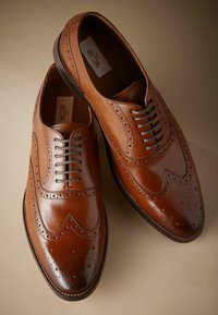 Ruske nahkasaapad brogue detailidega, terava nina ja paeltega disain. Omab sileda ja poleeritud tekstuuri ümarate servadega.