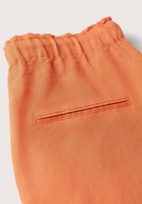 Gros plan sur un pantalon orange à taille élastique avec une poche passepoilée unique  à l'arrière, montrant la texture du tissu et les détails de couture.