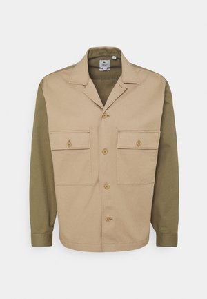 Zweifarbige beige und olivgrüne langärmelige Hemdjacke mit vorderer Knopfleiste, zwei mit Knöpfen verschlossenen Klappentaschen auf der Brust und einem Kragen.