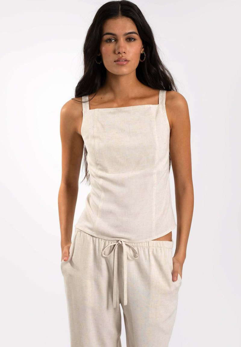 Top de mezcla de lino en beige claro con escote cuadrado y tirantes finos. La tela tiene una textura sutil. Combinado con pantalones holgados a juego.