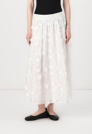 Gonna maxi bianca con ricami floreali e pompon texture, caratterizzata da una vita elastica e una silhouette fluida. Indossata con ballerine nere.