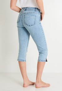Vaqueros capri azul claro con un diseño ajustado, cintura alta y dobladillo partido. Hechos de mezclilla, cuentan con bolsillos traseros y una textura ligeramente deslavada.