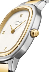 Reloj de metal en tonos dorado y plateado que presenta una esfera blanca, números romanos y un detalle de corona texturizada, con una forma de caja rectangular.